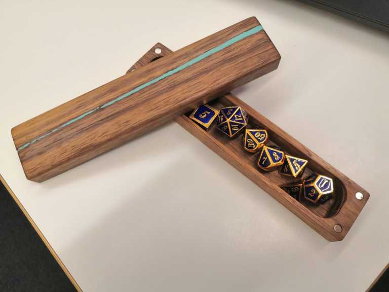Image of some metallic blue dice inside a walnut box with pale blue resin filling gaps.
